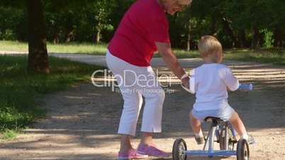 Grandmother assisting grandson to ride a bicycle