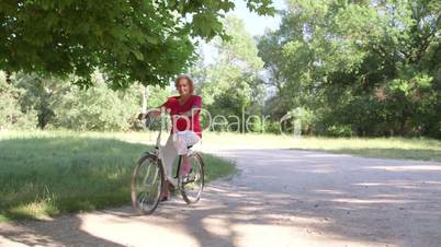 Active senior woman riding bicycle in park on sunny day