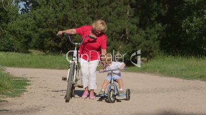 Grandmother with grandson riding bicycles in the summer park