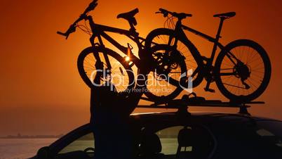 Cyclist attaching bikes to car roof carrier on summer beach