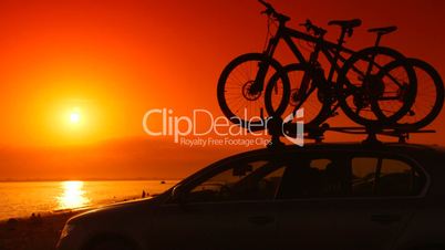 Car with mounted bicycles on summer beach at sunset