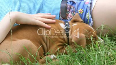 Tired child with puppy relaxing on grass in summer garden