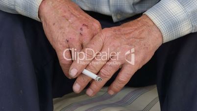 Worn wrinkled hands of senior man with cigarette