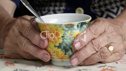 Wrinkled hands of senior woman with cup of drink close-up
