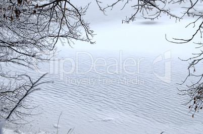 The view through the frame of the snowy branches on the frozen l