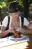 Blonde girl eats half chicken in a traditional beer garden
