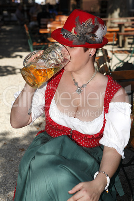 Woman in typical bavarian costume drinks beer