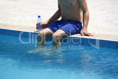 Attractive man with blue swimsuit and a bottle of water enjoys s