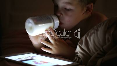Boy drinking milk from the bottle and looking at touchpad