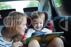 Boy holding book sitting in a car with mother