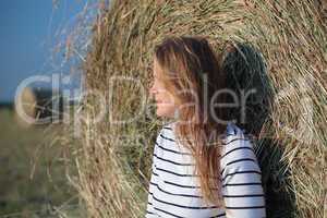 Young woman by the hay roll in the field