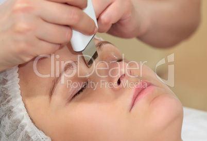 Woman under procedure of ultrasonic facial cleaning