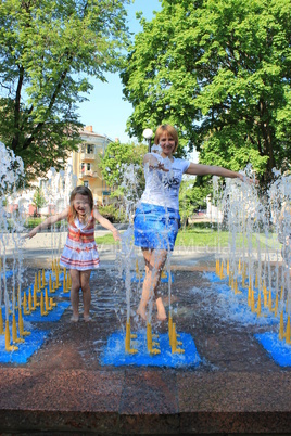 Mother and her daughter playing in the city fountain