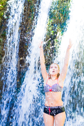 Young woman doing yoga exercise under waterfall