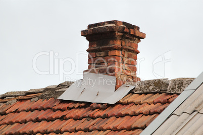 Old pipe from the furnace on the roof out shingles, on grey sky