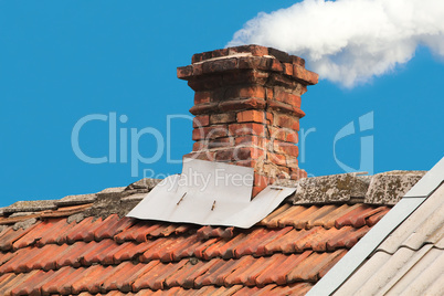 Old pipe from the furnace on the roof out shingles, on blue sky