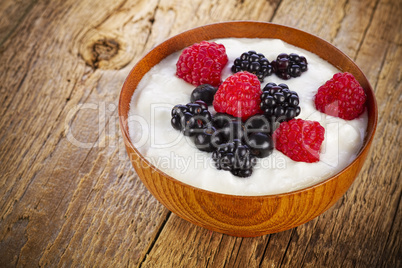 yogurt with forest berries in wooden bowl