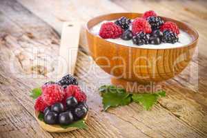 yogurt with wild berries in wooden bowl