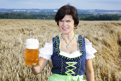 Bavarian woman in dirndl with beer mug in wheat field