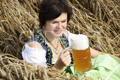 Bavarian woman in dirndl with beer mug in wheat field