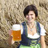 Bavarian woman in dirndl with beer mug in wheat field