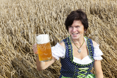 Bavarian woman in dirndl with beer mug in wheat field