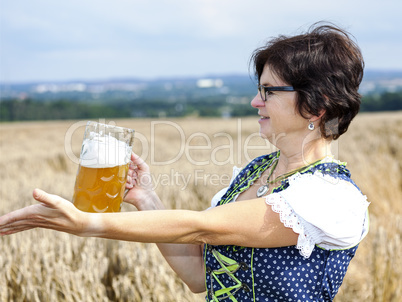 Bavarian woman in dirndl with beer mug in wheat field