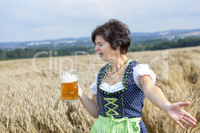 Bavarian woman in dirndl with beer mug in wheat field