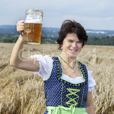 Bavarian woman in dirndl with beer mug in wheat field