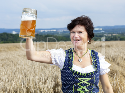 Bavarian woman in dirndl with beer mug in wheat field
