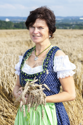 Bavarian woman in dirndl holds heads of grain in wheat field