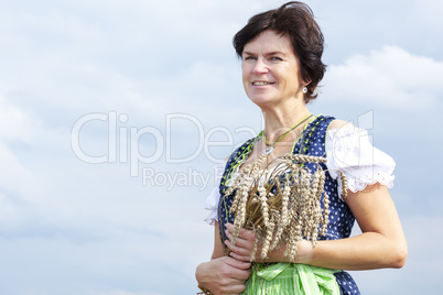 Bavarian woman in dirndl holds heads of grain in wheat field