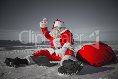 Santa Claus sitting in the snow with a laptop and looking away f