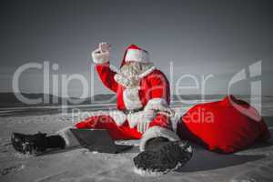 Santa Claus sitting in the snow with a laptop and looking away f