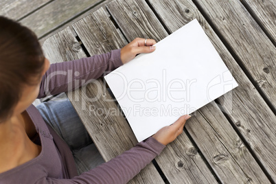 Young woman sitting at wooden table with a booklet with white Cover