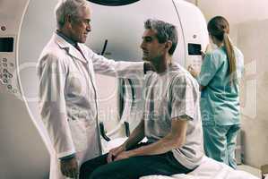 Senior male doctor explaining CT scanner exam to man in 40s. Fem