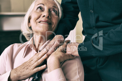 Senior woman on wheelchair taking her husband's hand