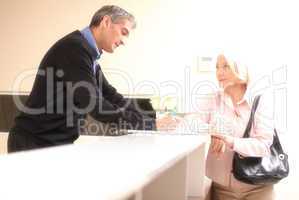 Senior female patient at hospital reception desk with man in 40s