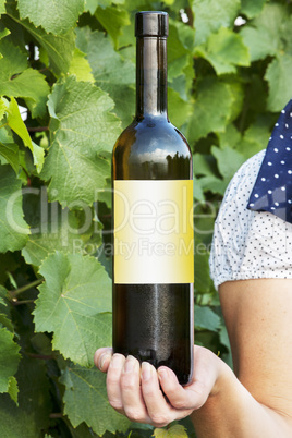 Woman holding bottle full of wine in vineyard