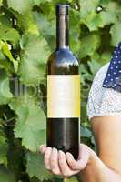 Woman holding bottle full of wine in vineyard