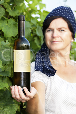 Woman holding bottle full of wine in vineyard