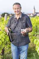 Man with wine bottle and glasses in vineyard