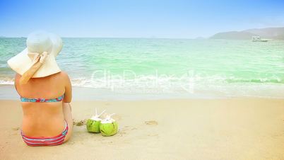 Woman and 2 coconuts on a sandy beach. Space for text.