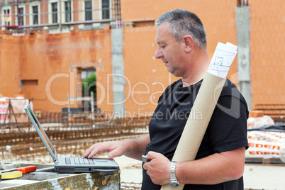 Civil engineer with blueprint and a laptop on site