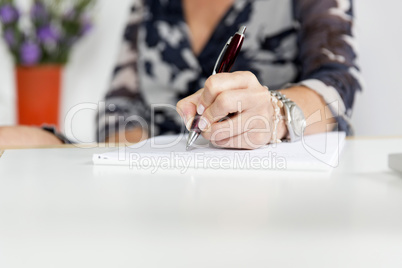 Hand (Frau) schreibend mit Kugelschreiber und Notizblock