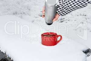 Hand filling in winter landscape cup with hot drink