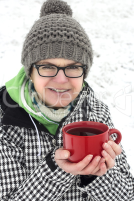 Woman standing in snowy landscape and keeps hot teacup