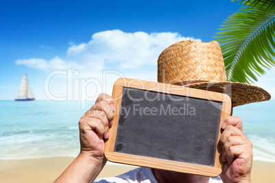 Mann hält am Strand leere Schiefertafel hoch