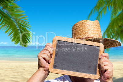 Mann hält am Strand leere Schiefertafel hoch