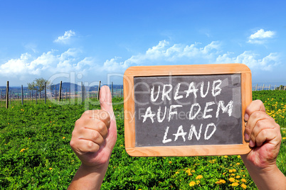 Hände halten Tafel mit Text: Urlaub auf dem Land